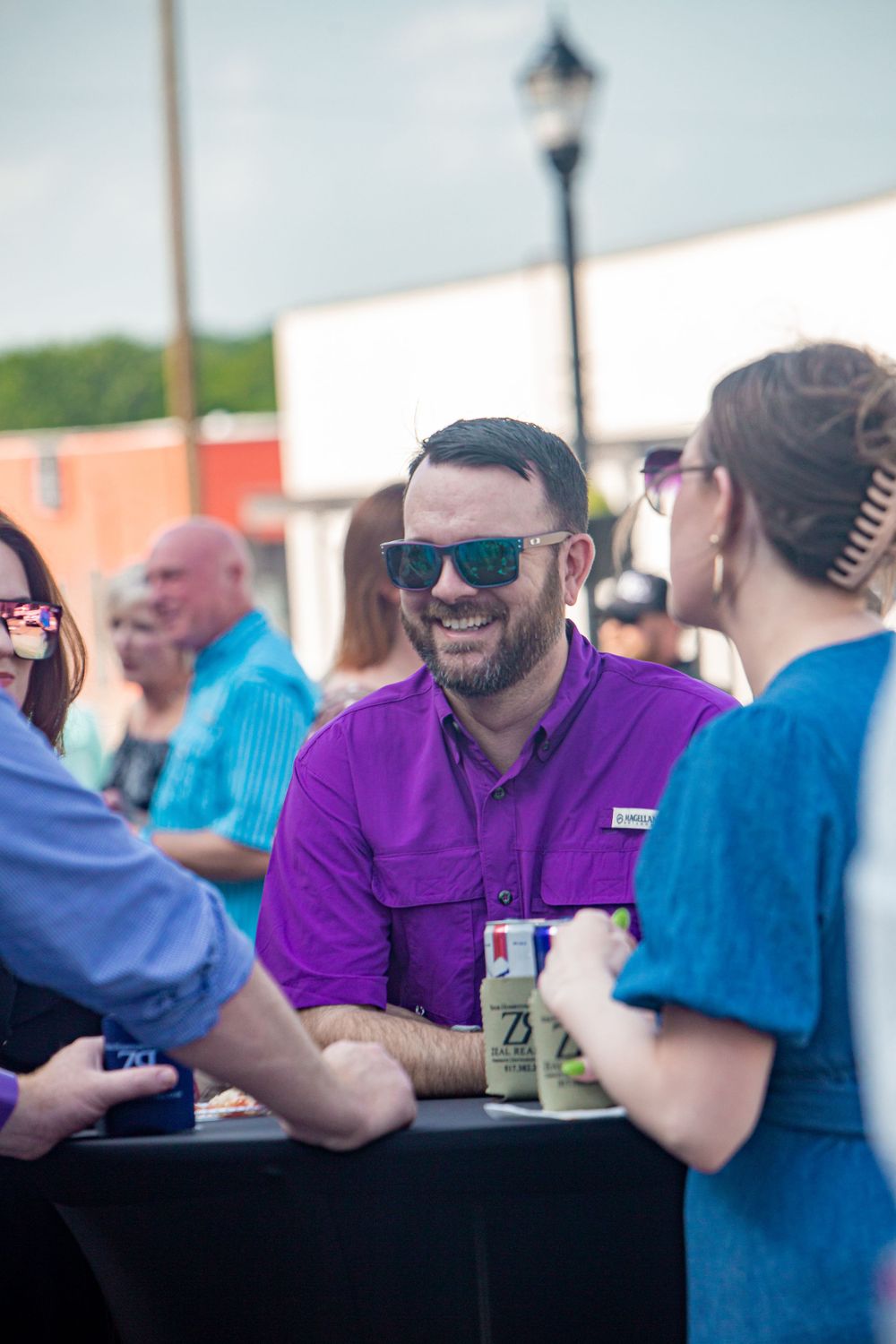 A group of people in purple and blue shirts enjoying conversation at an outdoor gathering.