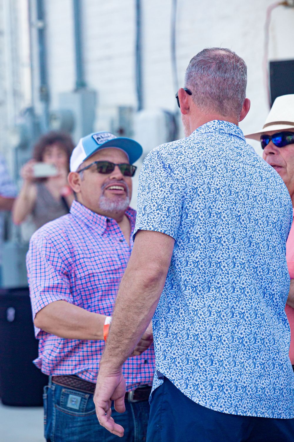 People in patterned shirts and sunglasses mingling at an outdoor social event.