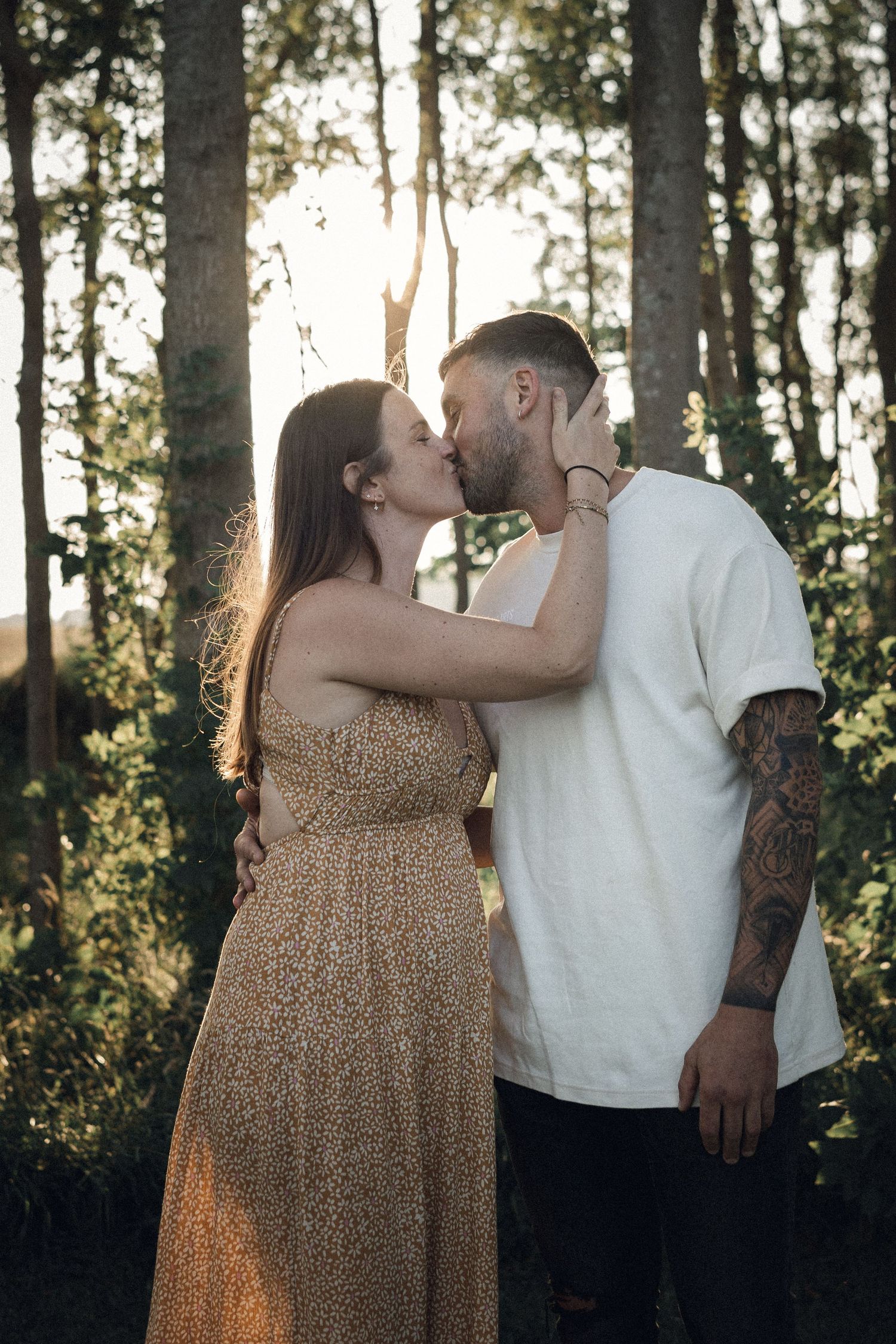 Intimate moment between couple kissing in sunlit forest setting.