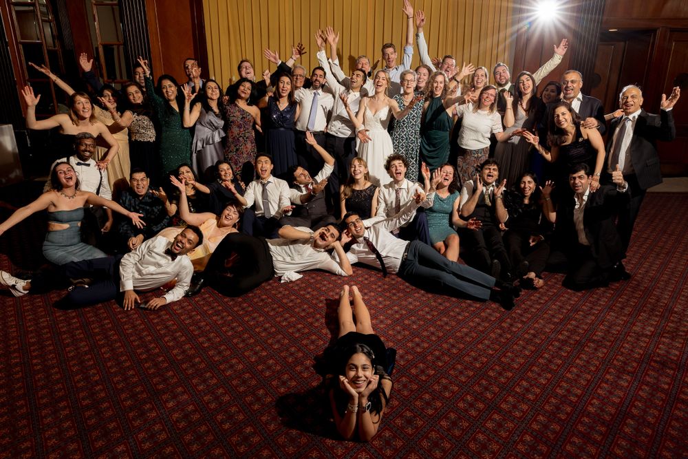 Wedding guests lay on red carpet dance floor while photographer captures unique party shot from above at reception.