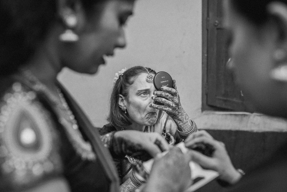 Black and white photo showing people getting ready in front of a mirror with makeup application being done.