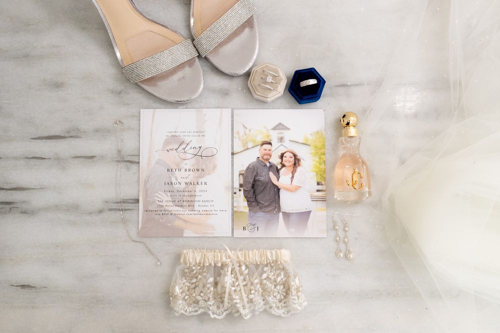 Flat lay of wedding accessories including shoes, invitations and delicate lace details on marble surface.