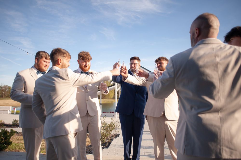 Groomsmen in light colored suits celebrating outdoors under blue sky.
