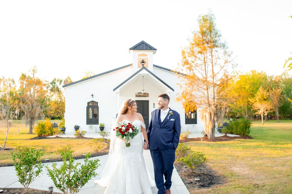 Wedding couple standing in front of a quaint white church during autumn.