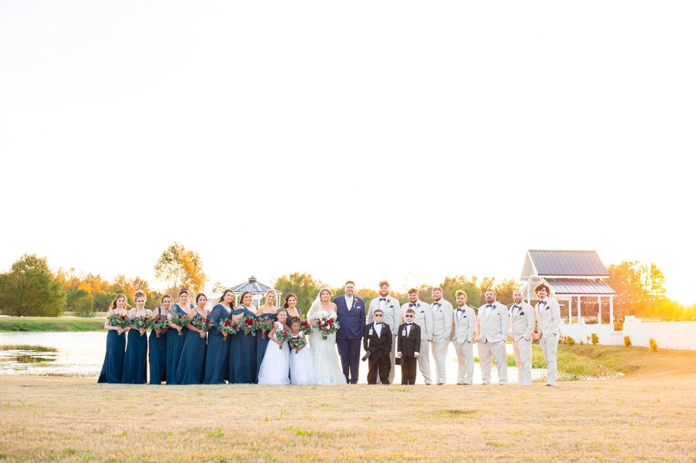 Wedding party in navy and white poses by the water at sunset.