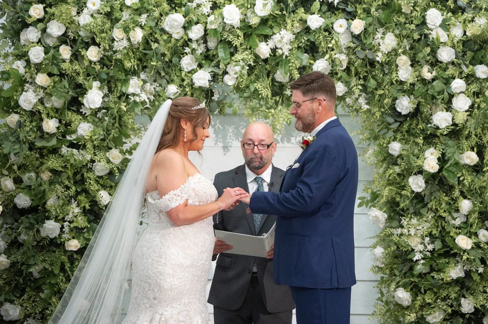 Wedding ceremony under an elegant white floral arch with roses and greenery.