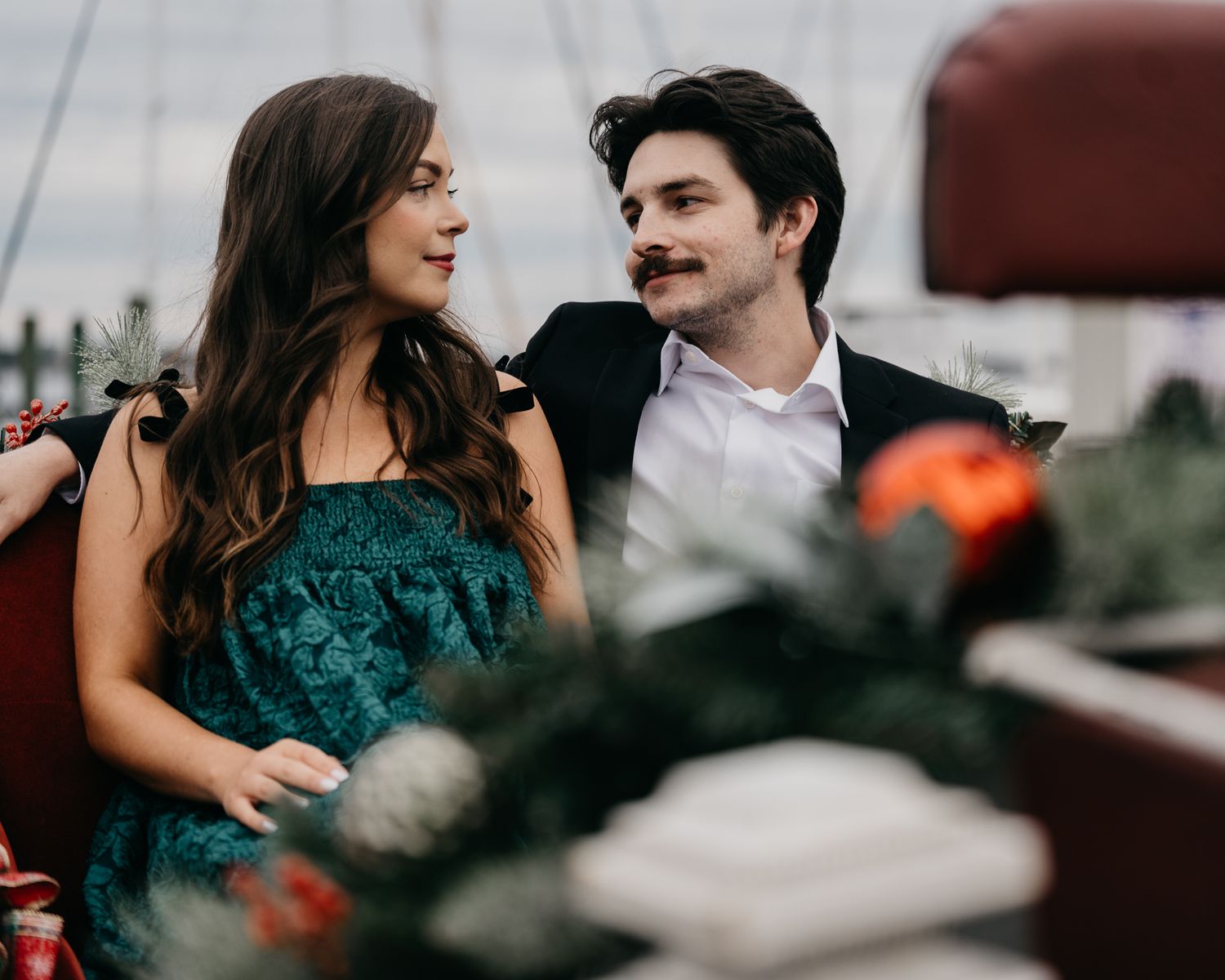 A romantic couple shares a joyful moment while seated among greenery and flowers.