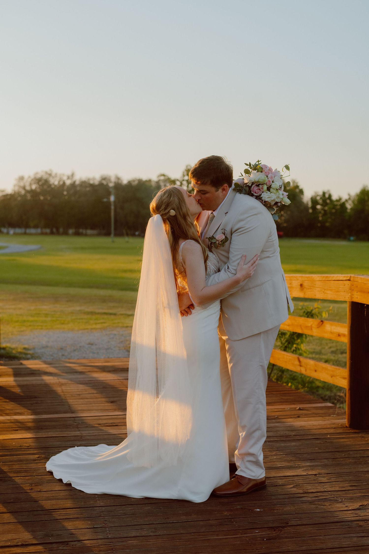 Romantic sunset wedding photo with bride in white dress holding autumn bouquet against ancient stone ruins backdrop.