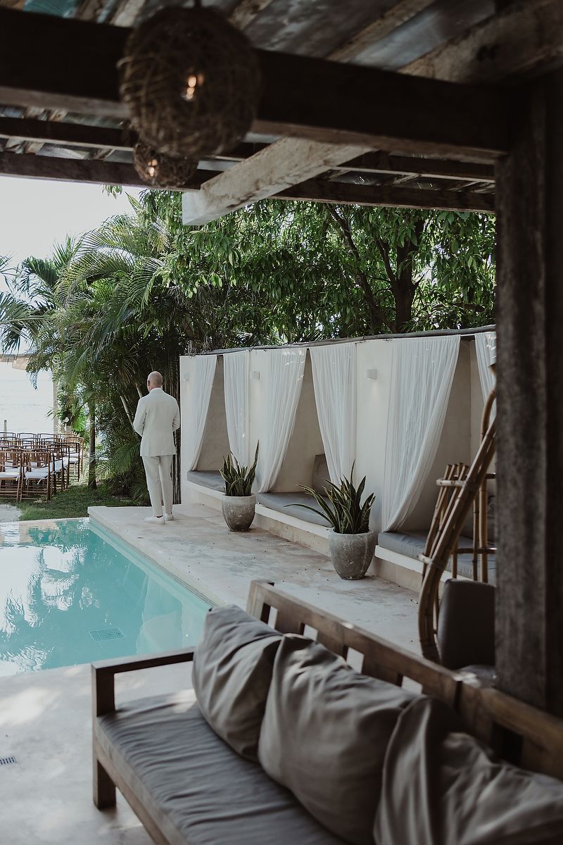 Elegant poolside cabana with white curtains, lush tropical greenery, and a couple in white attire at a luxury resort.