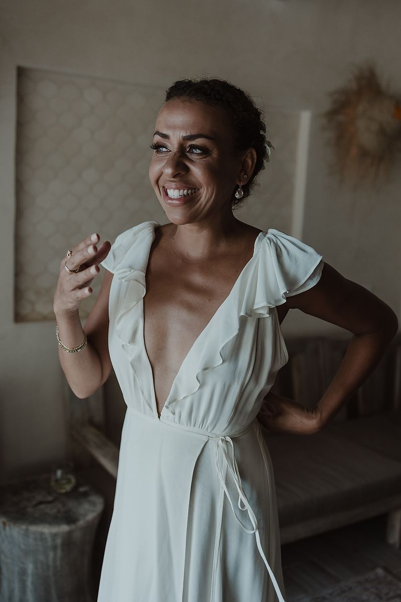 Smiling bride in white deep V-neck ruffle dress posing indoors on her wedding day.