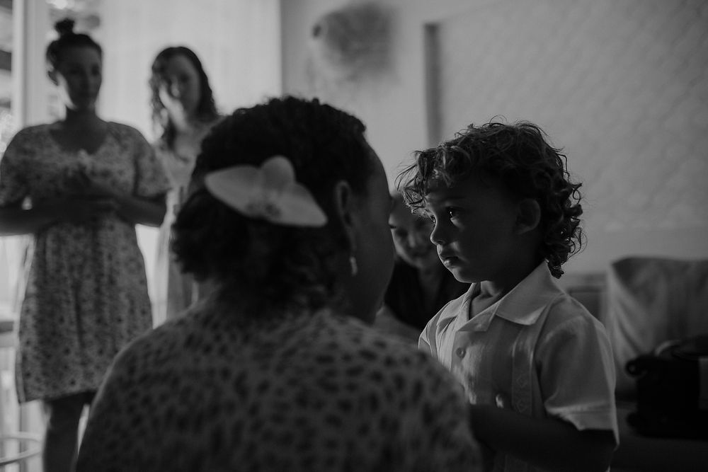 Black and white photo of a curly-haired child looking up at a woman indoors, with two women standing in the background.