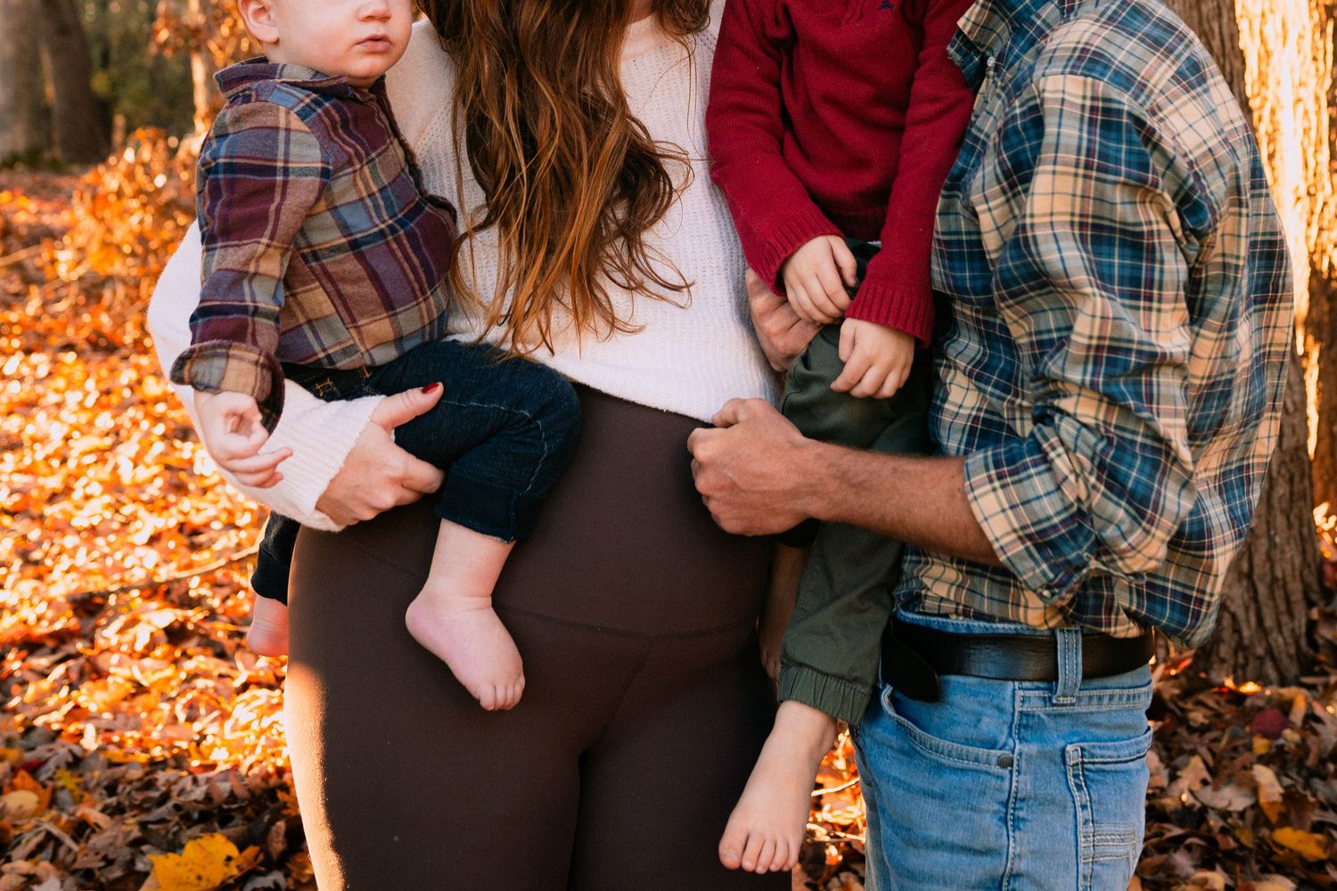 Parents in casual fall clothing holding a baby outdoors among autumn leaves.