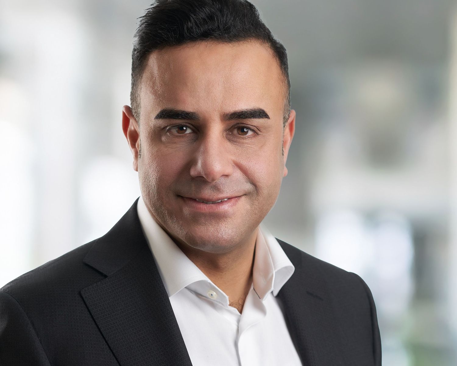 Professional headshot portrait of someone in a dark suit jacket and white dress shirt against a blurred office background by Evan Will