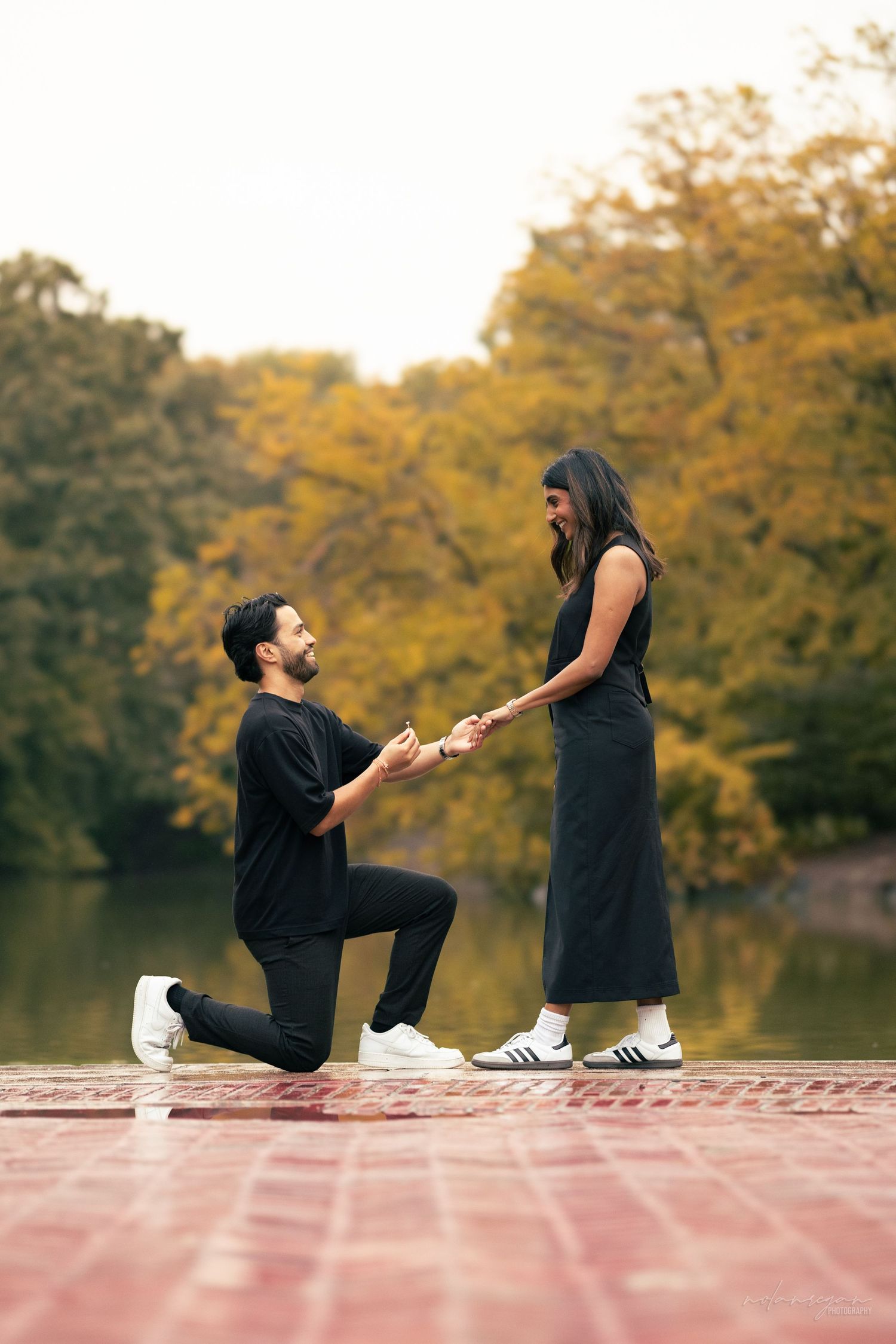 A romantic proposal scene with two people on a wooden deck by a lake in autumn.