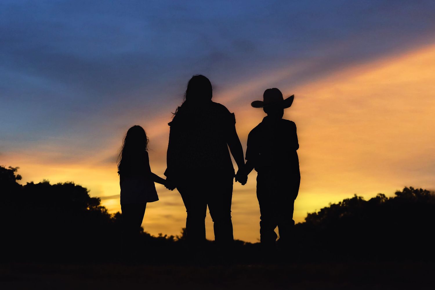 Silhouette of three people holding hands at sunset against colorful sky.