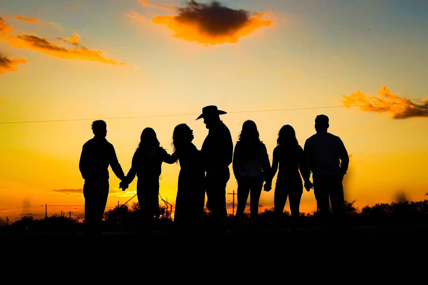 Row of people holding hands in silhouette against a golden sunset sky.