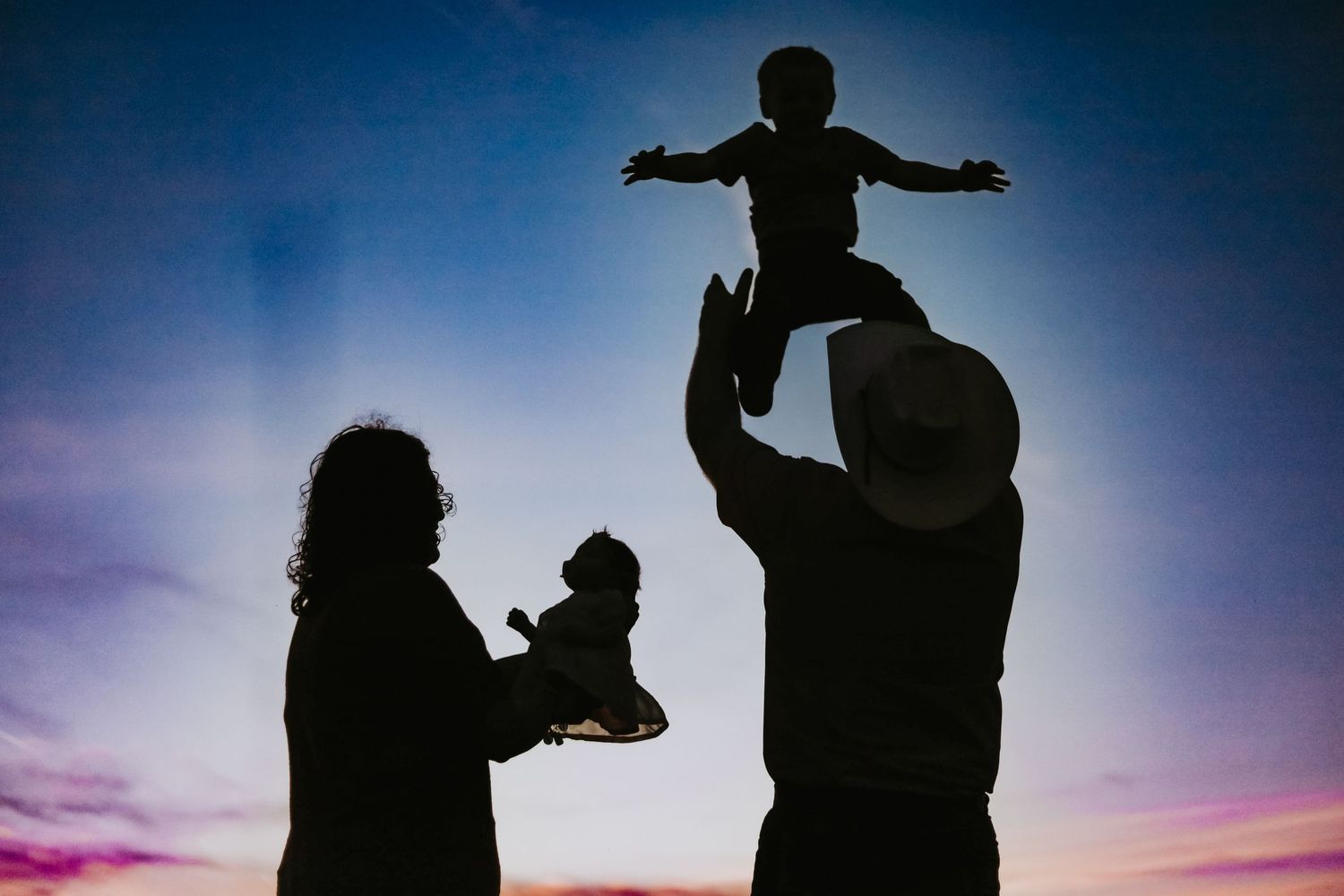 Silhouette of family playing together against purple sunset sky.