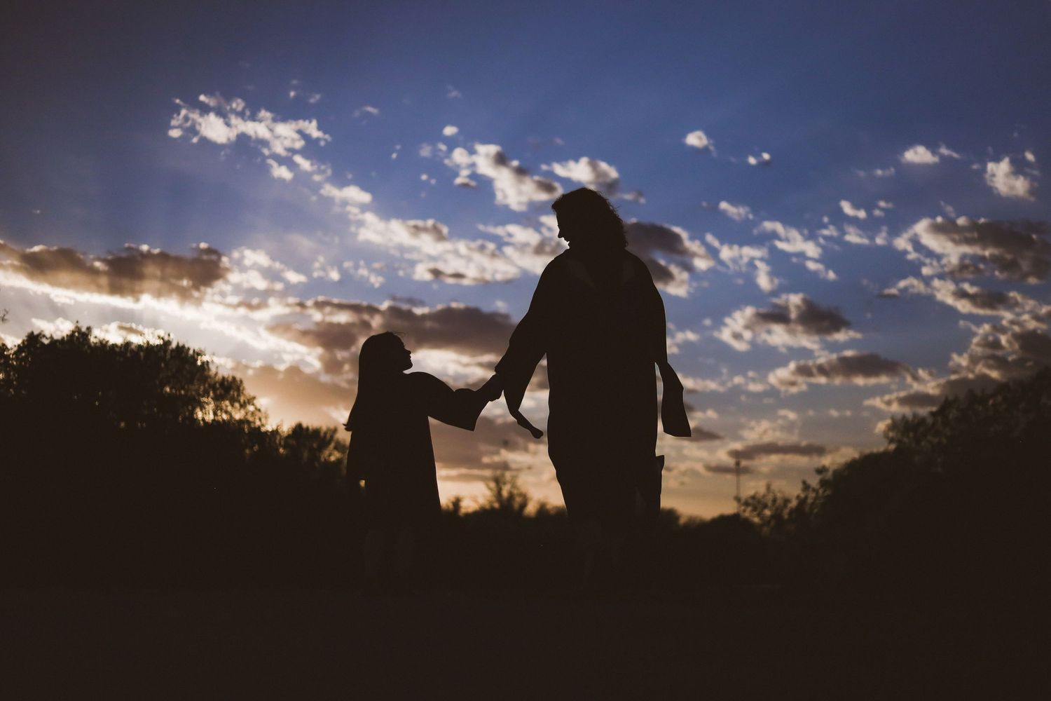 Two figures walking together at sunset with dramatic cloudy sky.