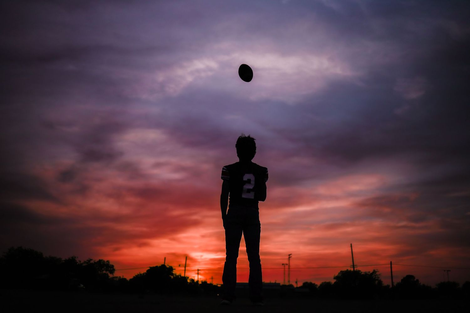 Silhouette of a person tossing a ball against a dramatic purple sunset sky.