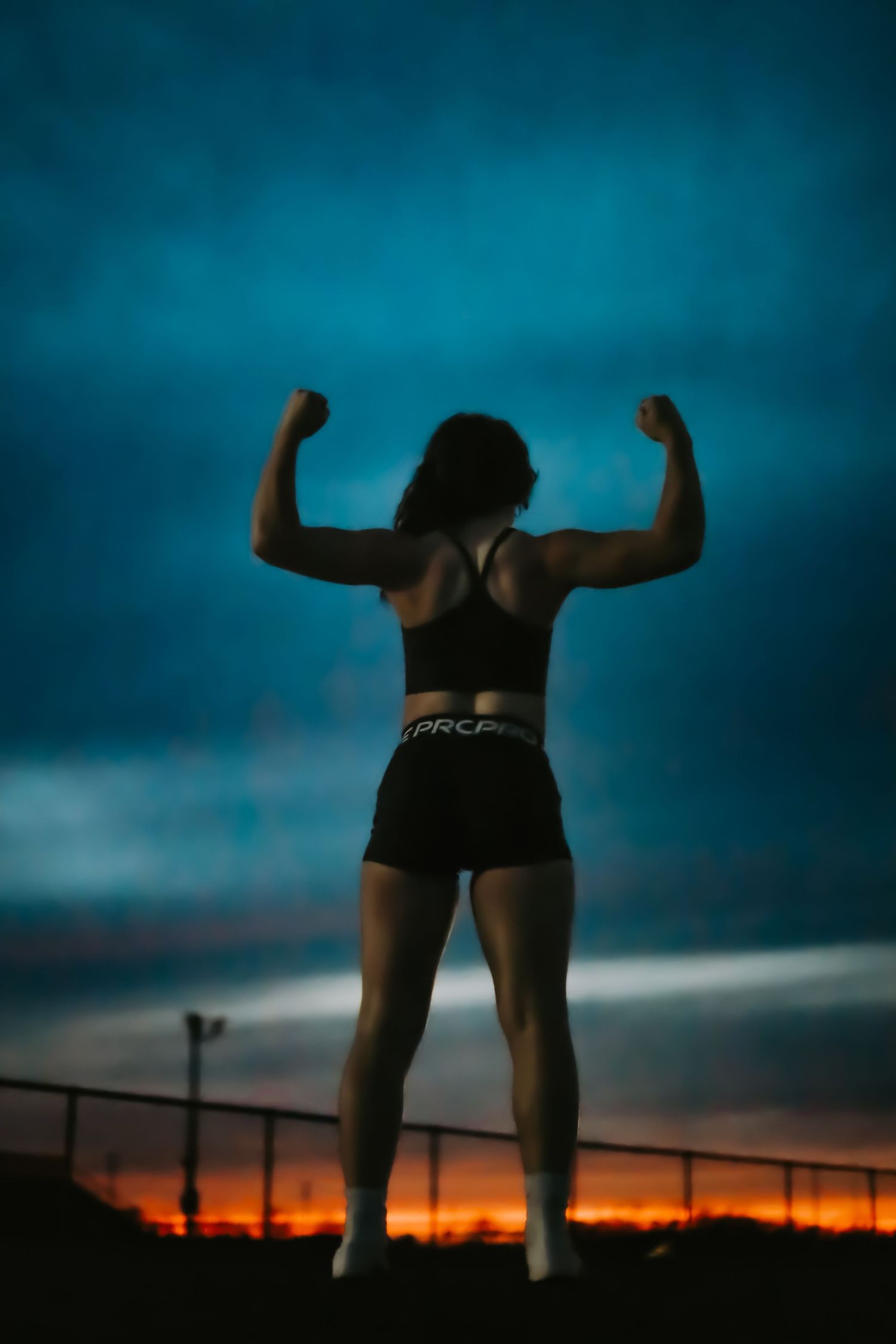 Athletic figure flexing muscles against dramatic blue and orange sunset sky.