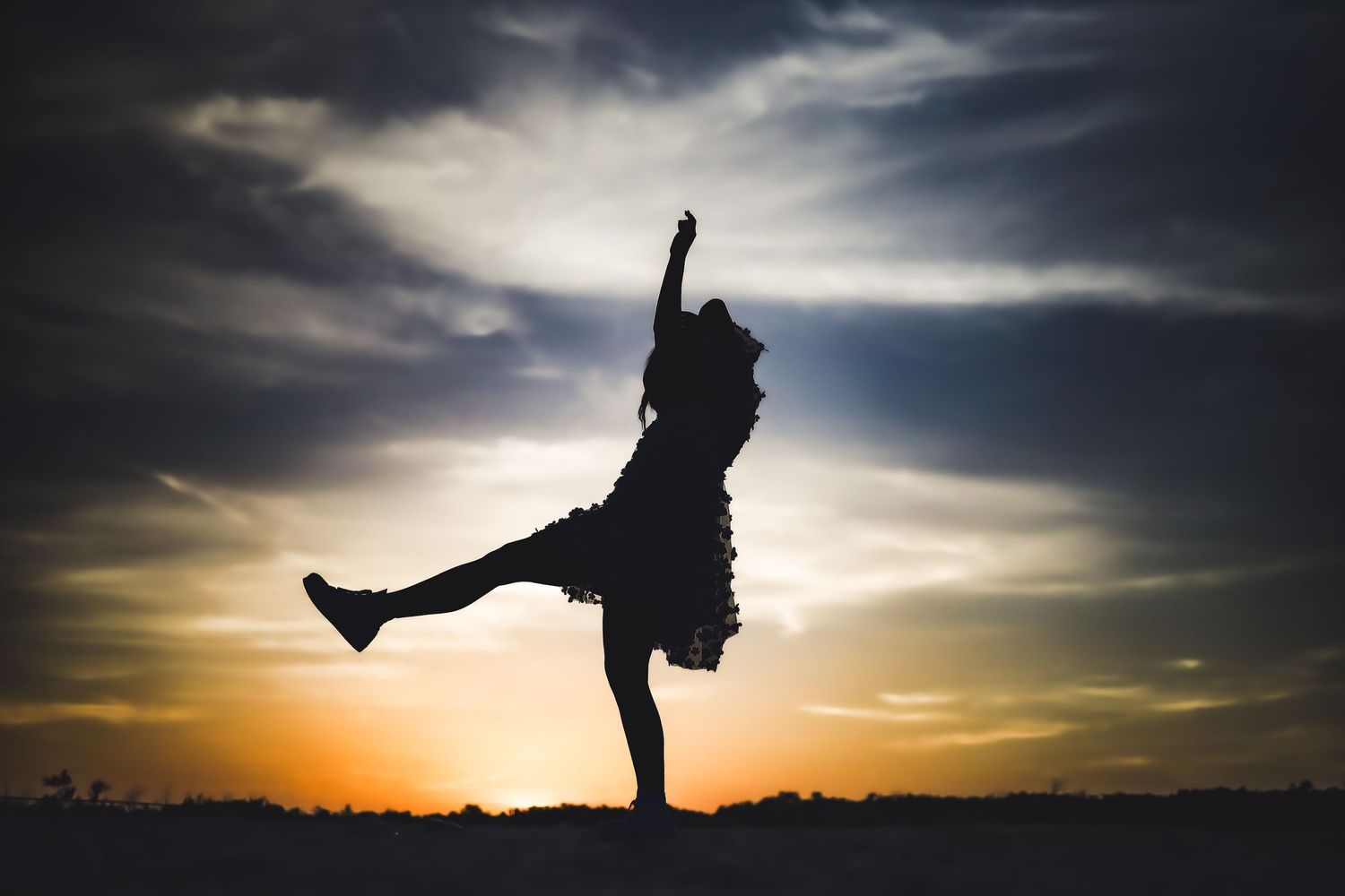 Dynamic silhouette of person dancing against golden sunset.