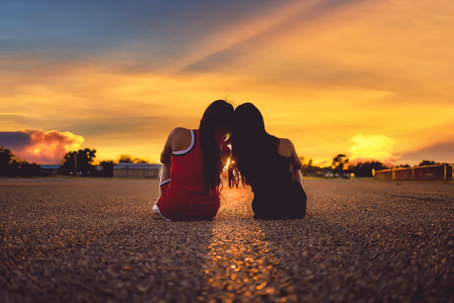 Two silhouettes sitting close together watching a golden sunset on the ground.