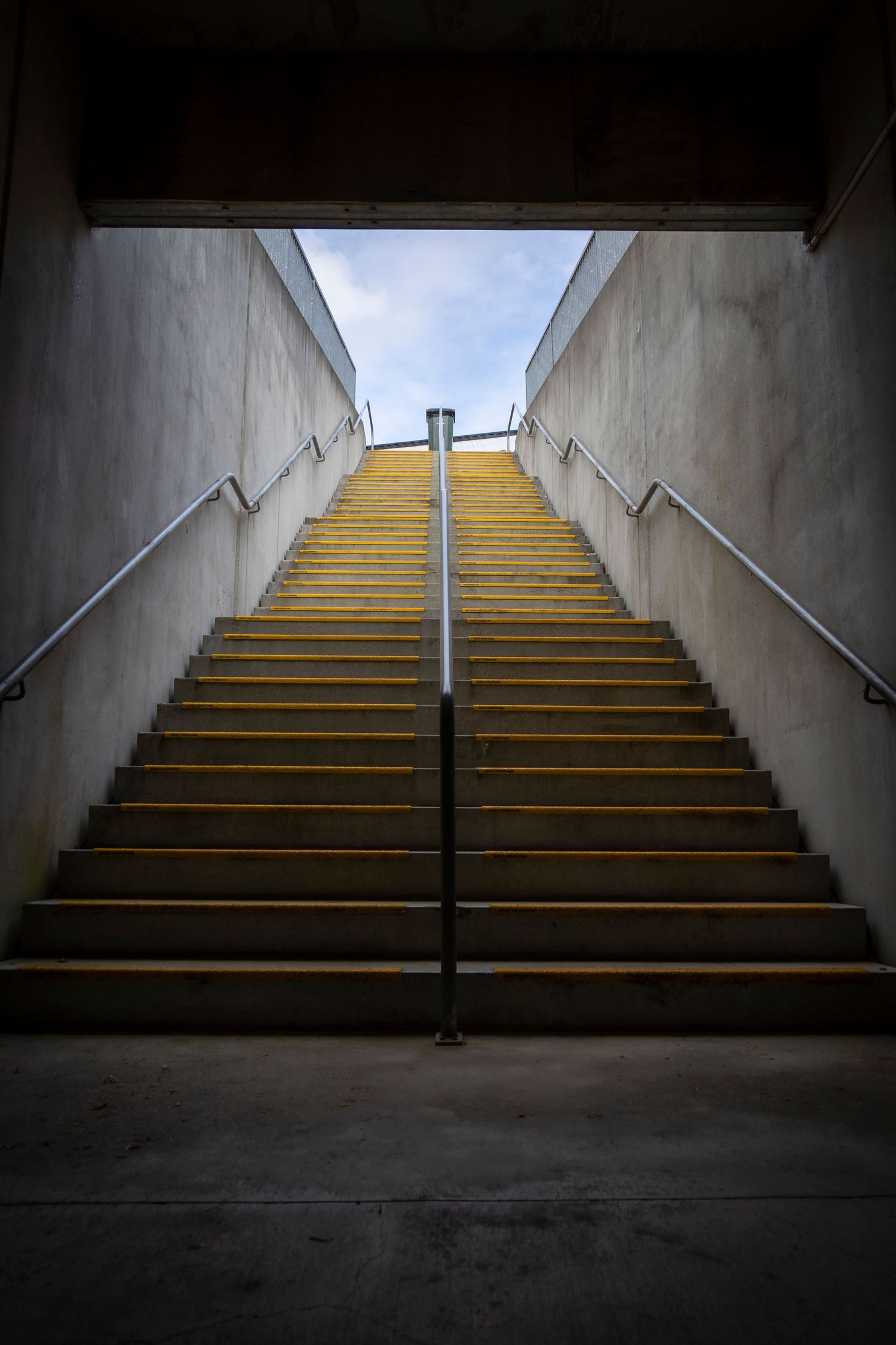Concrete stairwell with yellow steps and natural light above.