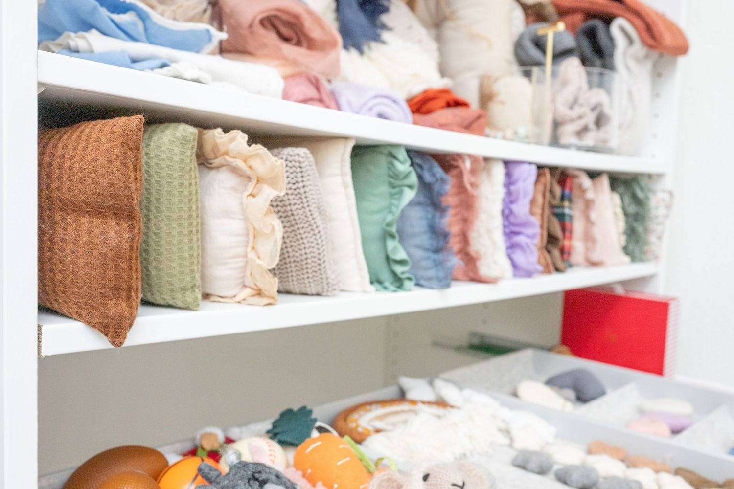 Neatly organized closet shelves displaying folded clothes, blankets, and linens in various pastel colors.