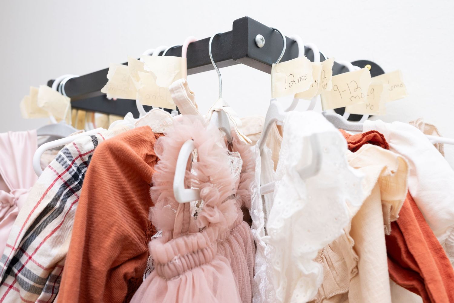 Pastel and earth-toned clothing collection displayed on white hangers against a light background.