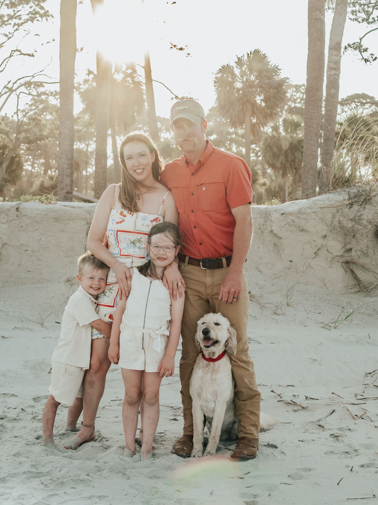 Family sitting together on sandy ground among palm trees at sunset.