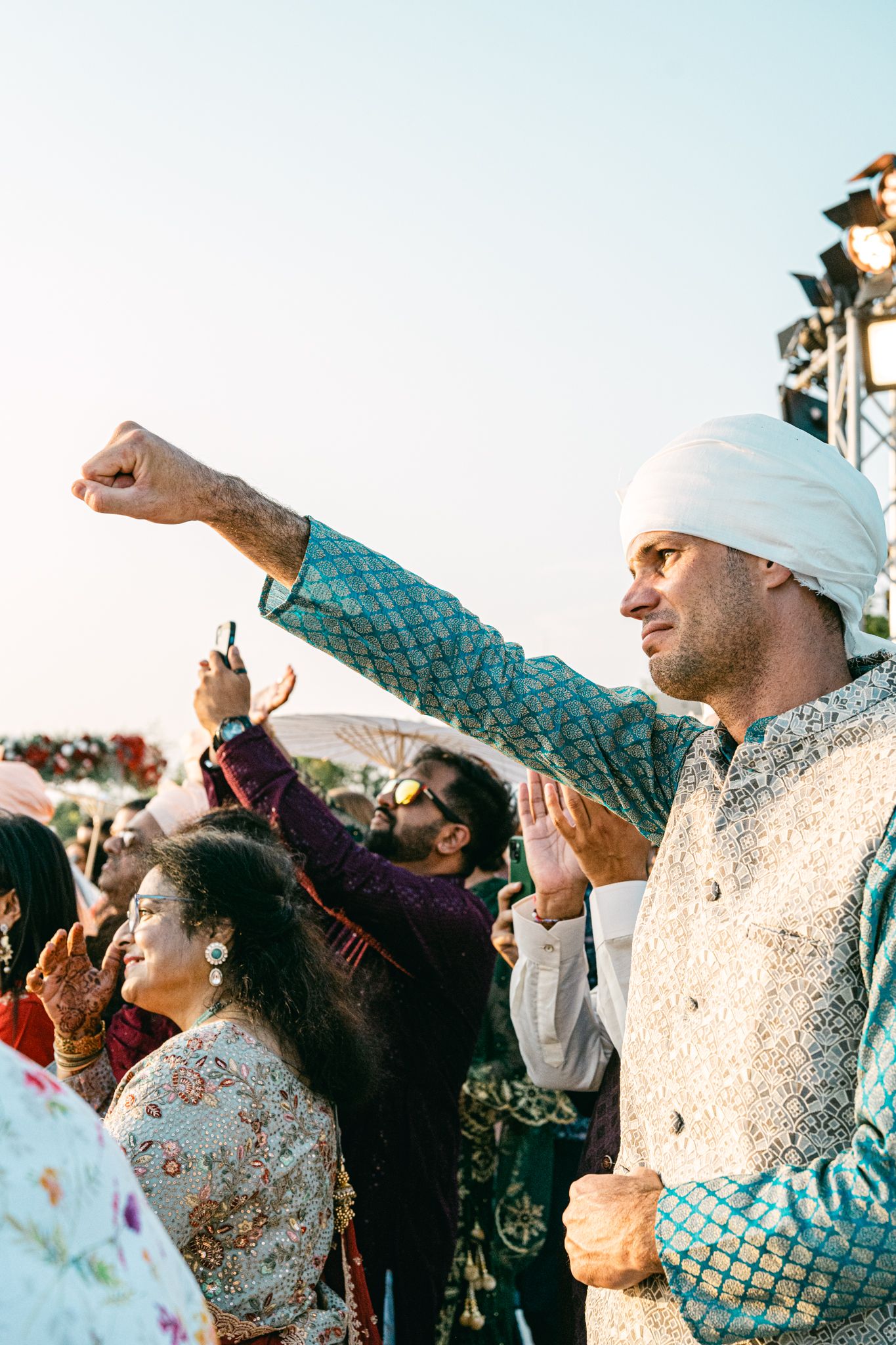 Wedding guests in traditional attire celebrate joyfully during an outdoor celebration.