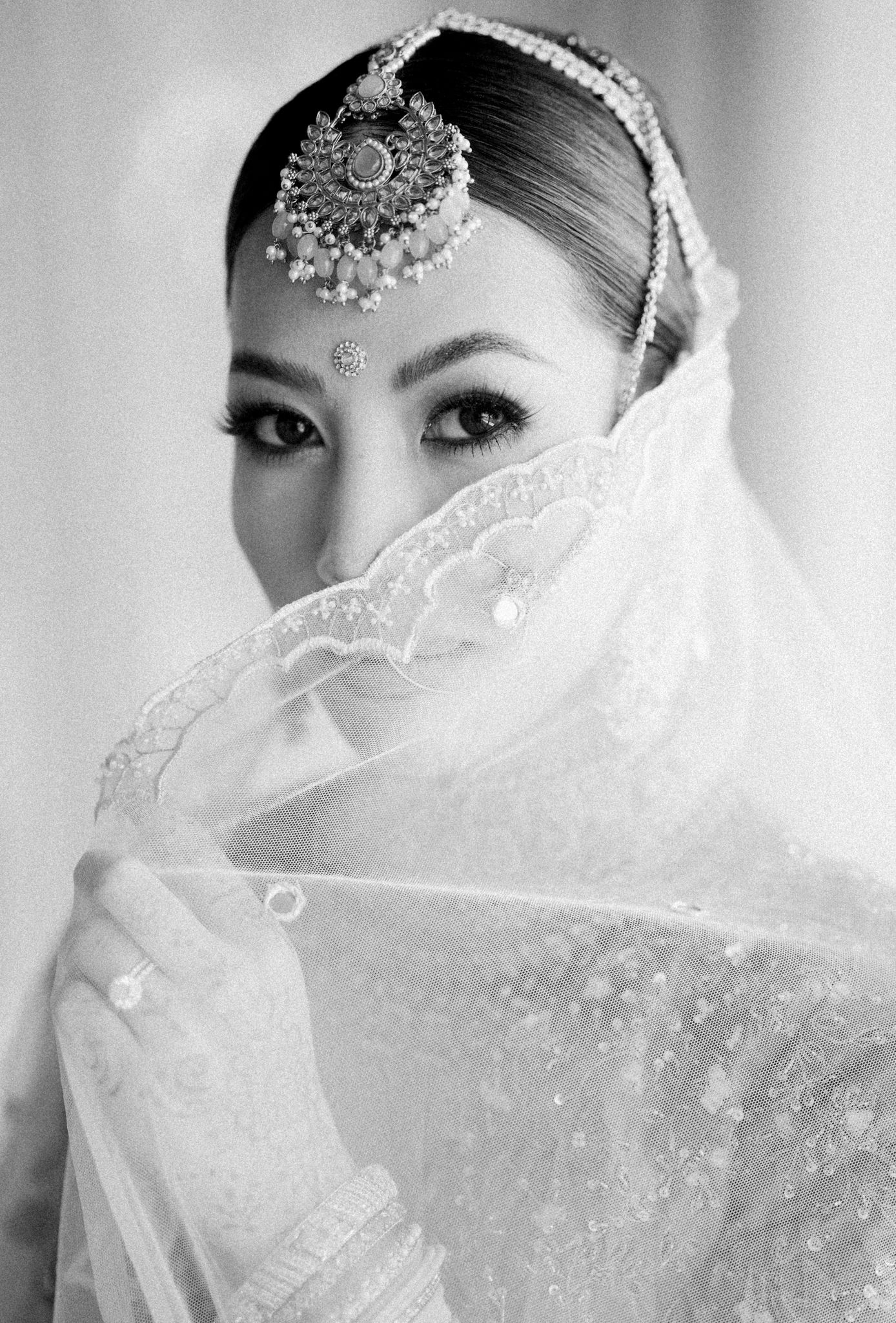 Black and white portrait of South Asian bridal jewelry and veil details.