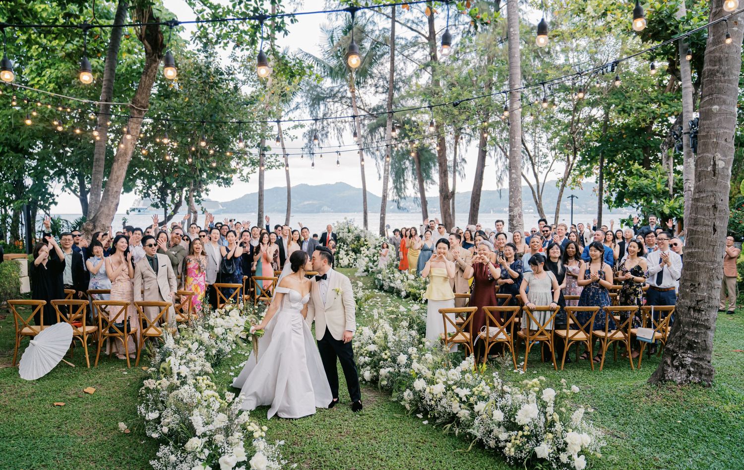 Newlyweds celebrate with guests at an outdoor garden wedding ceremony with white floral decorations.