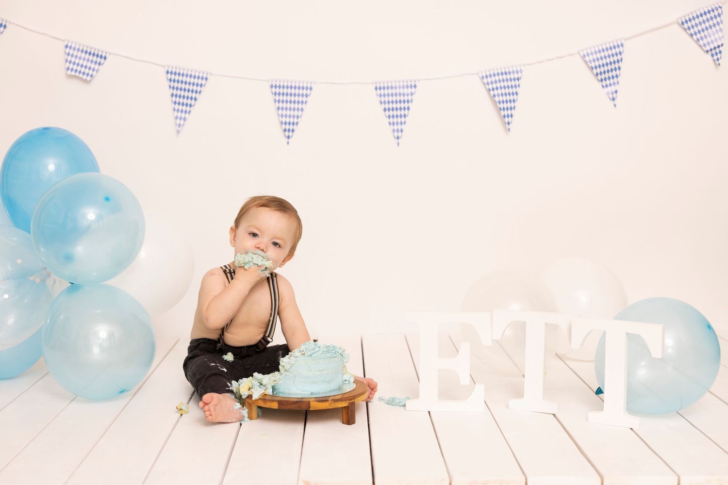 Baby wearing pink headband sits in white wooden barrel prop with peach roses for newborn photography session.