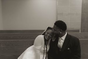 A black and white photo captures an intimate moment between a couple in a church setting.