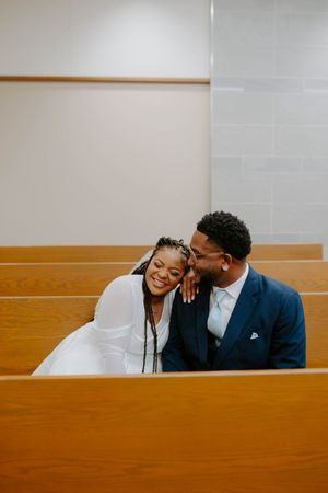 A couple laughs together while sitting in a church pew during their wedding day.