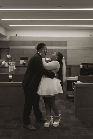 A black and white wedding photo captures an intimate moment between newlyweds in a courthouse.