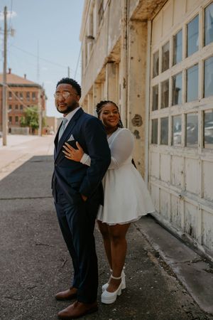A couple shares a playful moment in front of a white building exterior.