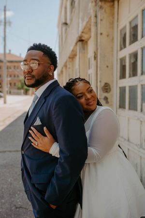 A couple embraces lovingly against a light-colored wall.
