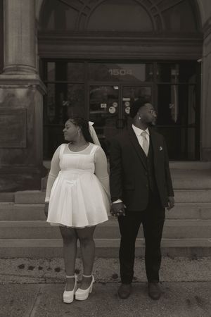 A couple stands together in formal attire outside a historic building.