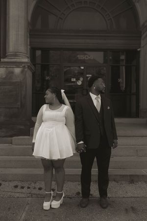 A couple poses together in front of an architectural facade.