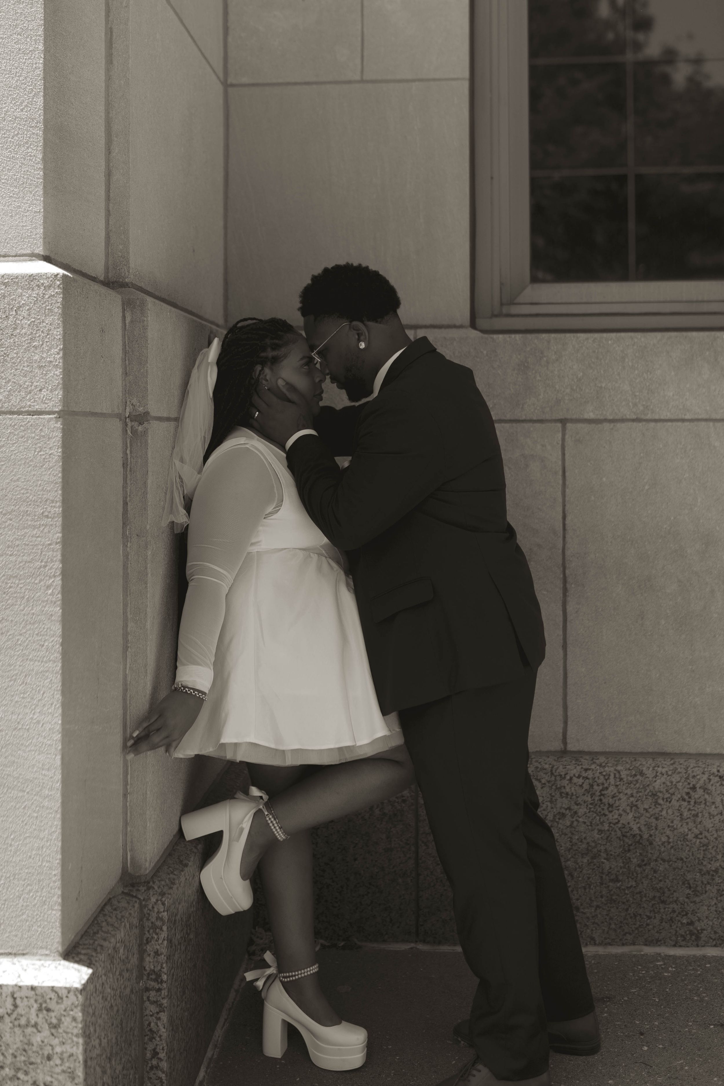 A romantic black and white sequence showing a couple embracing near a building wall.