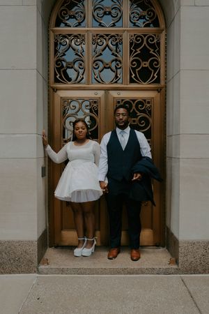A family poses in formal wear in front of ornate wooden doors with decorative ironwork.