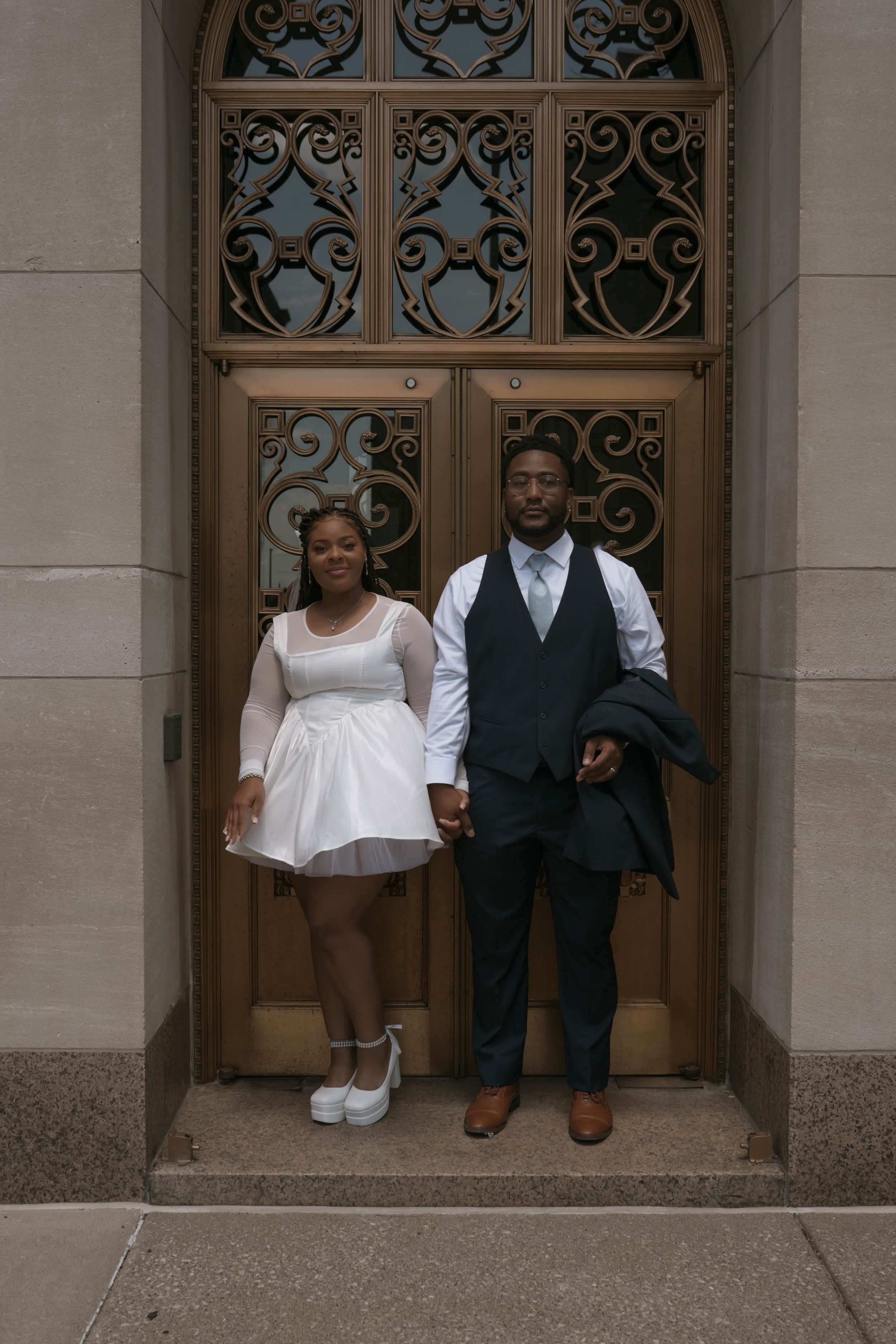 A couple poses playfully in front of ornate doors at their wedding venue.