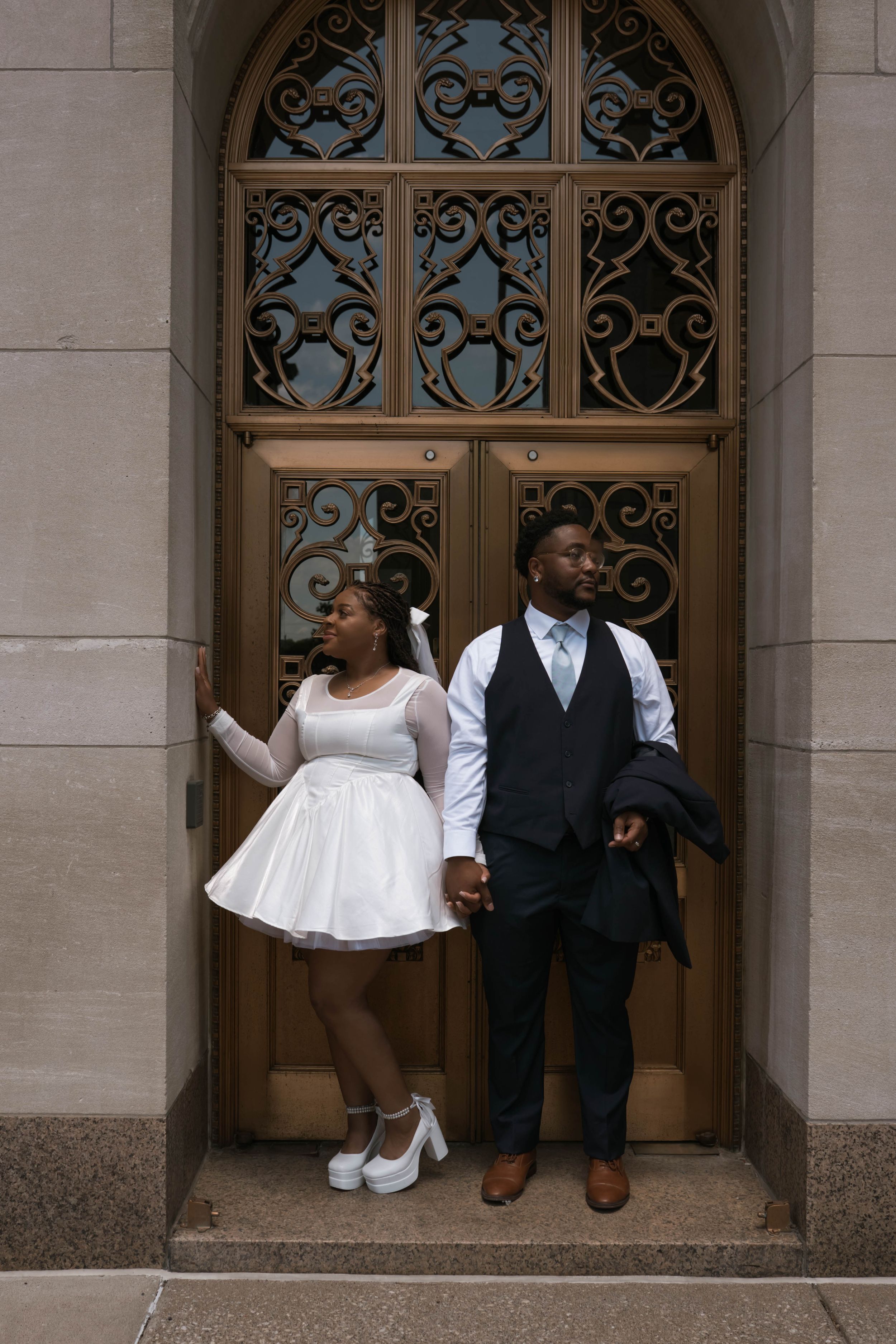 Wedding couple shares candid moments while seated in front of decorative doors.