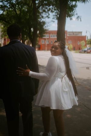 A couple in black and white outfits share a tender moment outdoors under tree shadows.