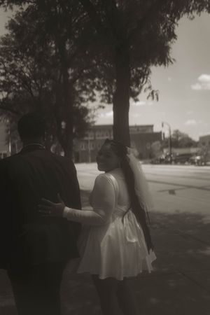 Two people stroll along a tree-lined path in formal wear.