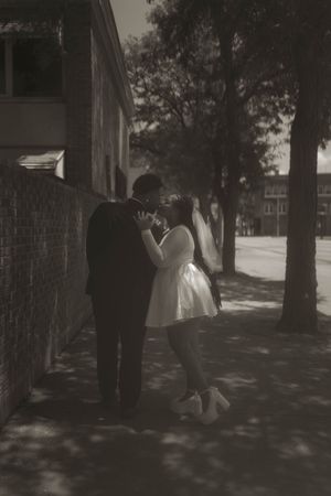 A couple walks through a shaded outdoor area near brick buildings.