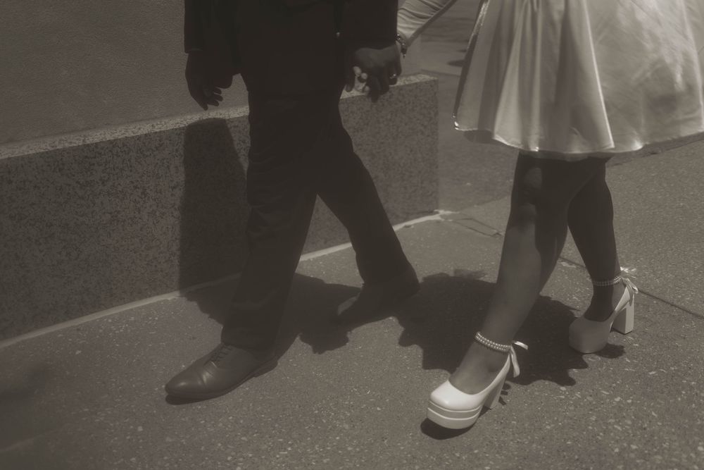 Close-up view of formal shoes and dress hemlines on pavement.