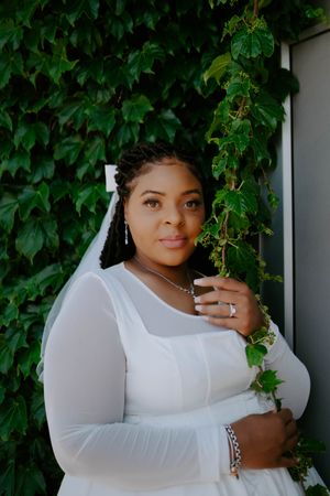 Portrait in front of ivy-covered wall with soft natural lighting and white clothing.